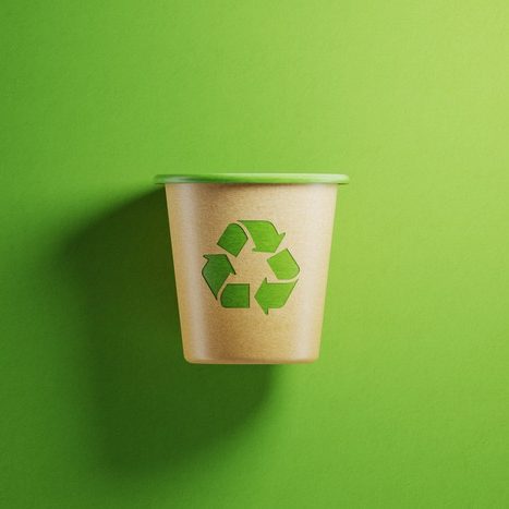Garbage bin made of recycled paper on Green background. There is a recycling symbol on the waste bin. Horizontal composition with copy space.